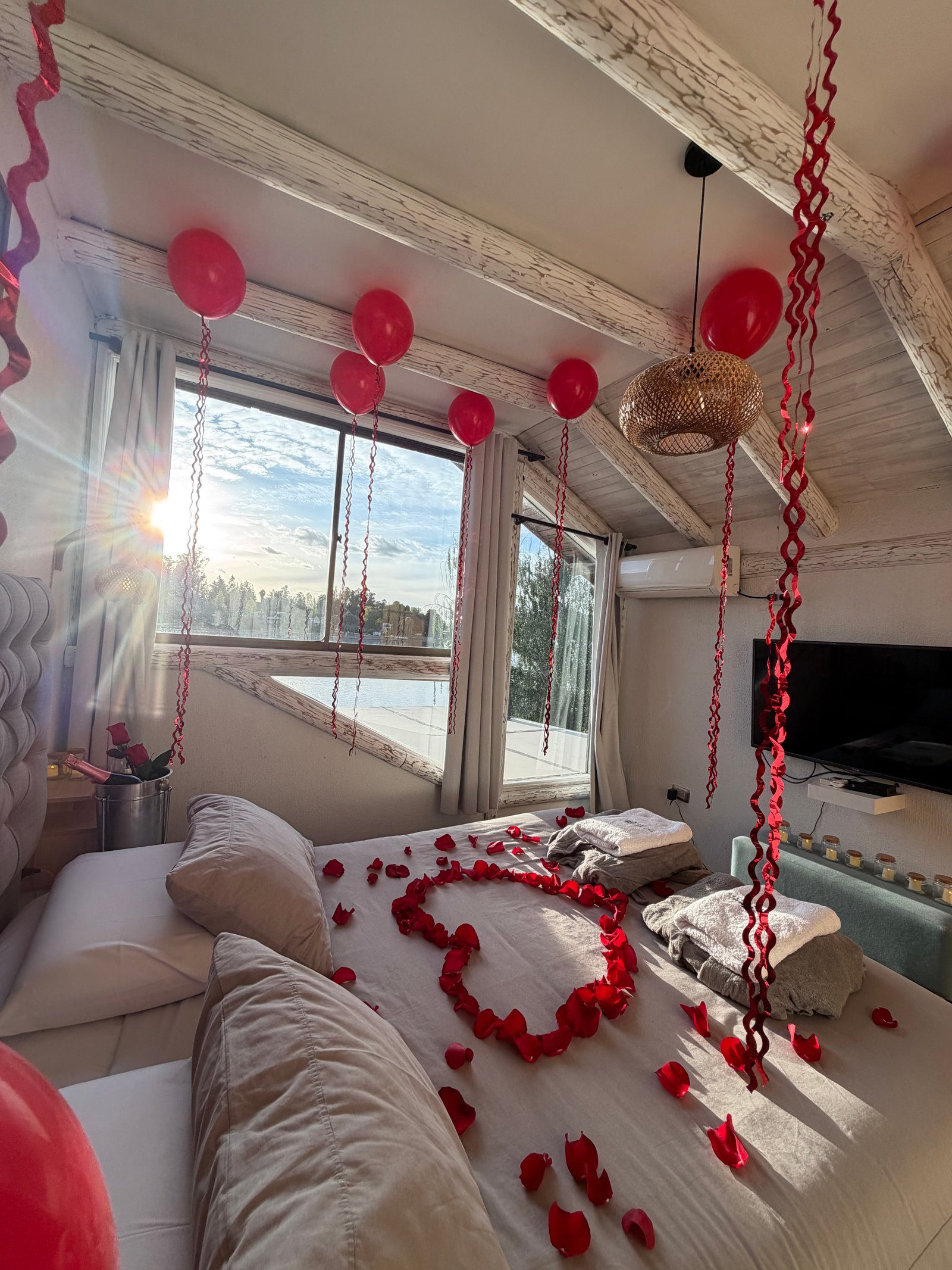 Pieza de Orilla decorada con globos rojos y pétalos en forma de corazón sobre la cama